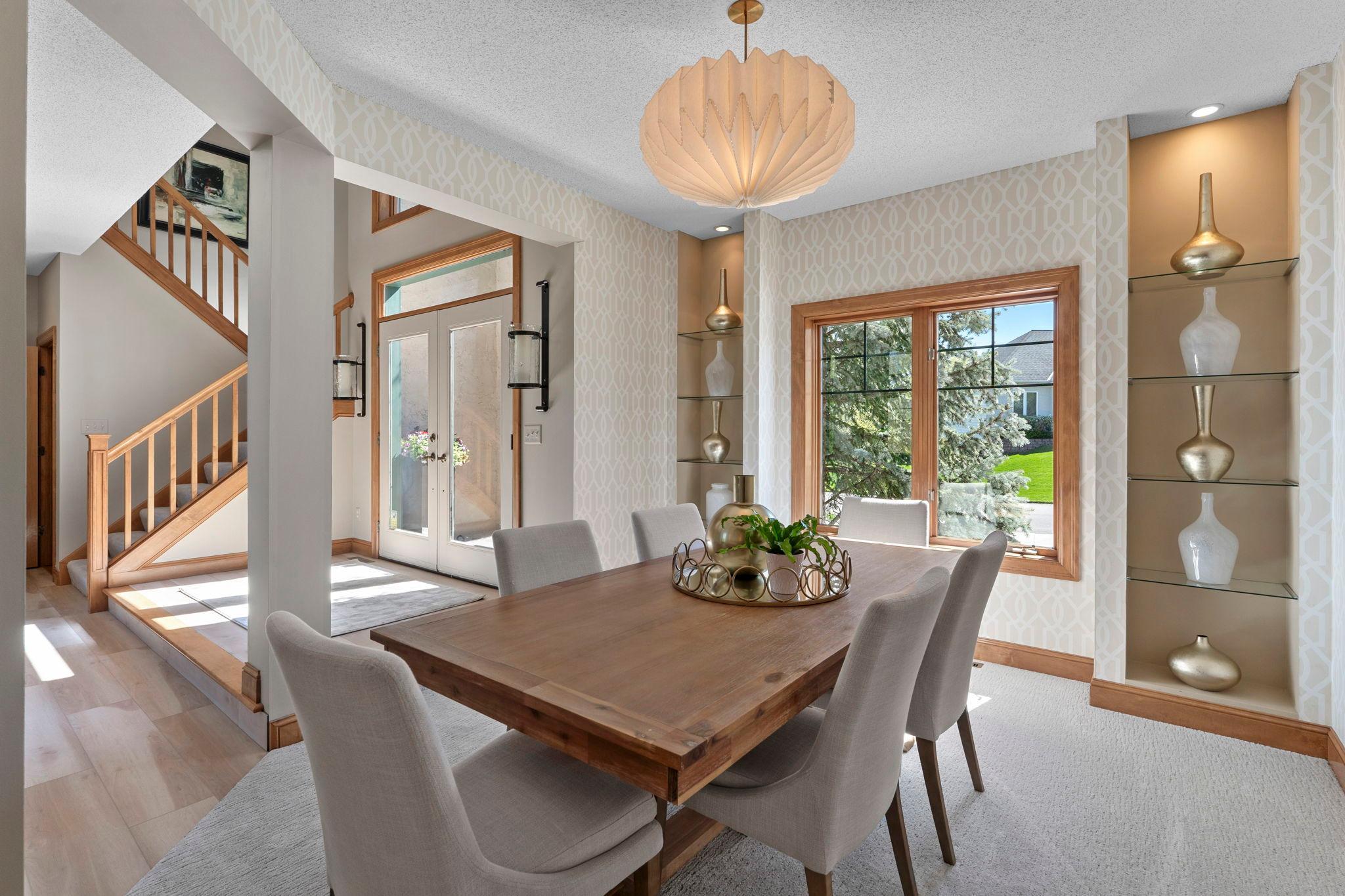 The main level is a formal dining room featuring carpeting, stylish wallpaper, a decorative light fixture, built-in shelving, and a front-facing window that fills the space with natural light, creating a setting ideal for more formal gatherings.