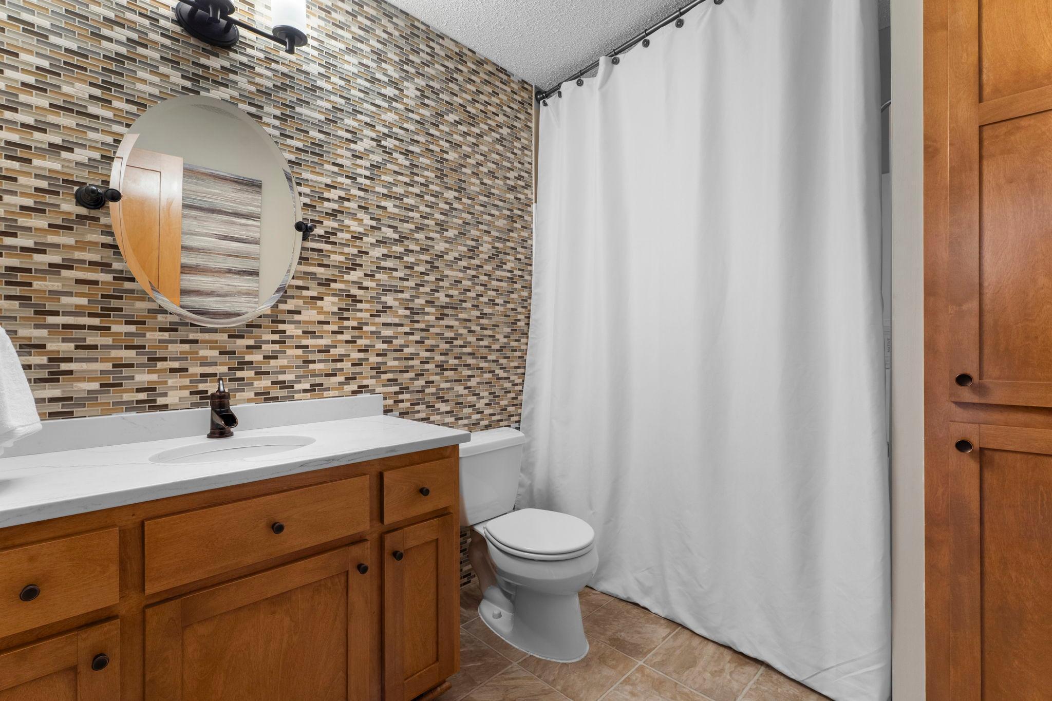 Just steps away is a shared full bathroom with a tile accent wall, quartz countertop vanity, linen storage, and a tub/shower combination.