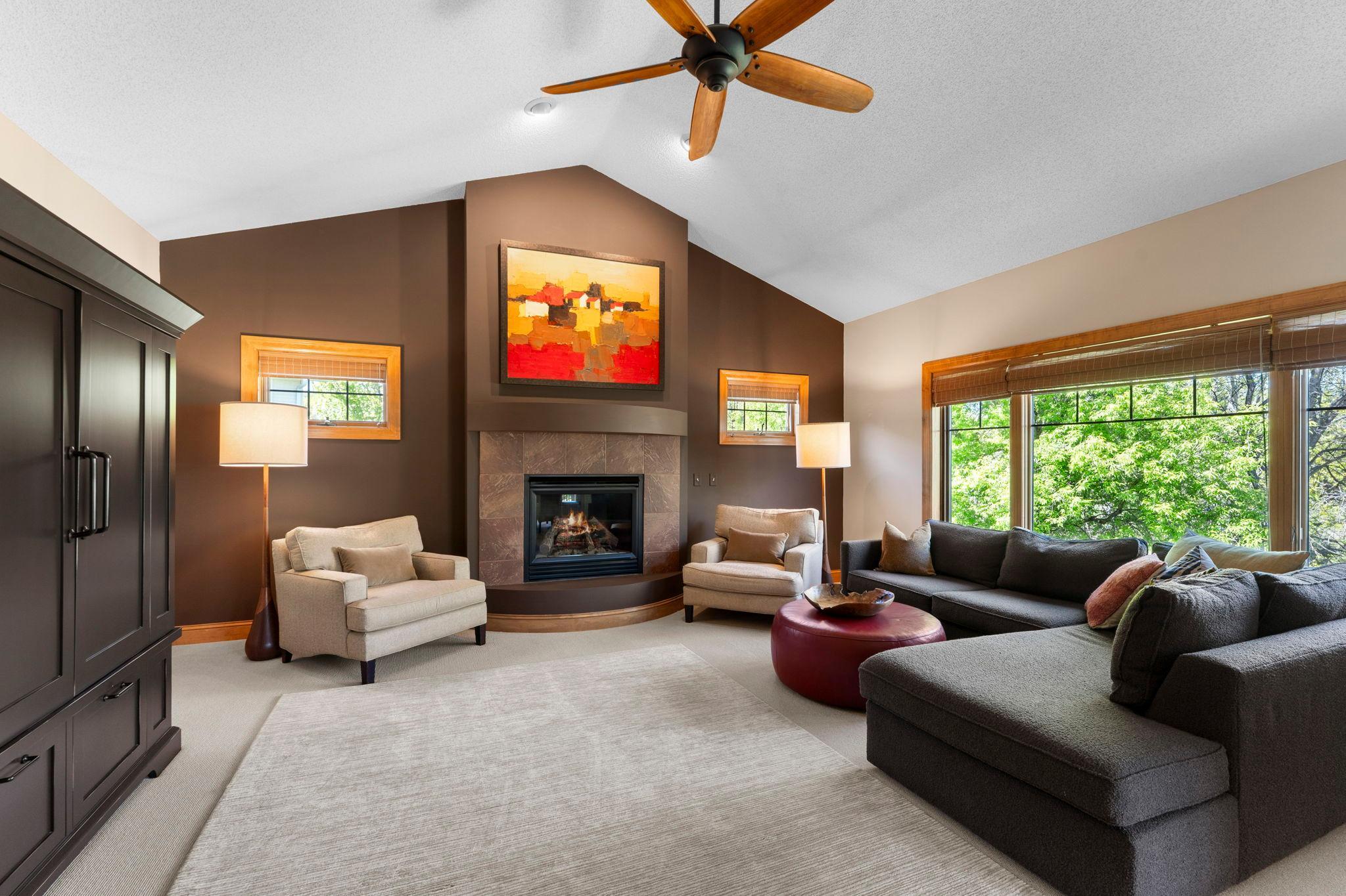 Adjacent to the kitchen and dining area is a comfortable living room with carpeting, vaulted ceilings, a ceiling fan, large windows, and a gas-burning fireplace.