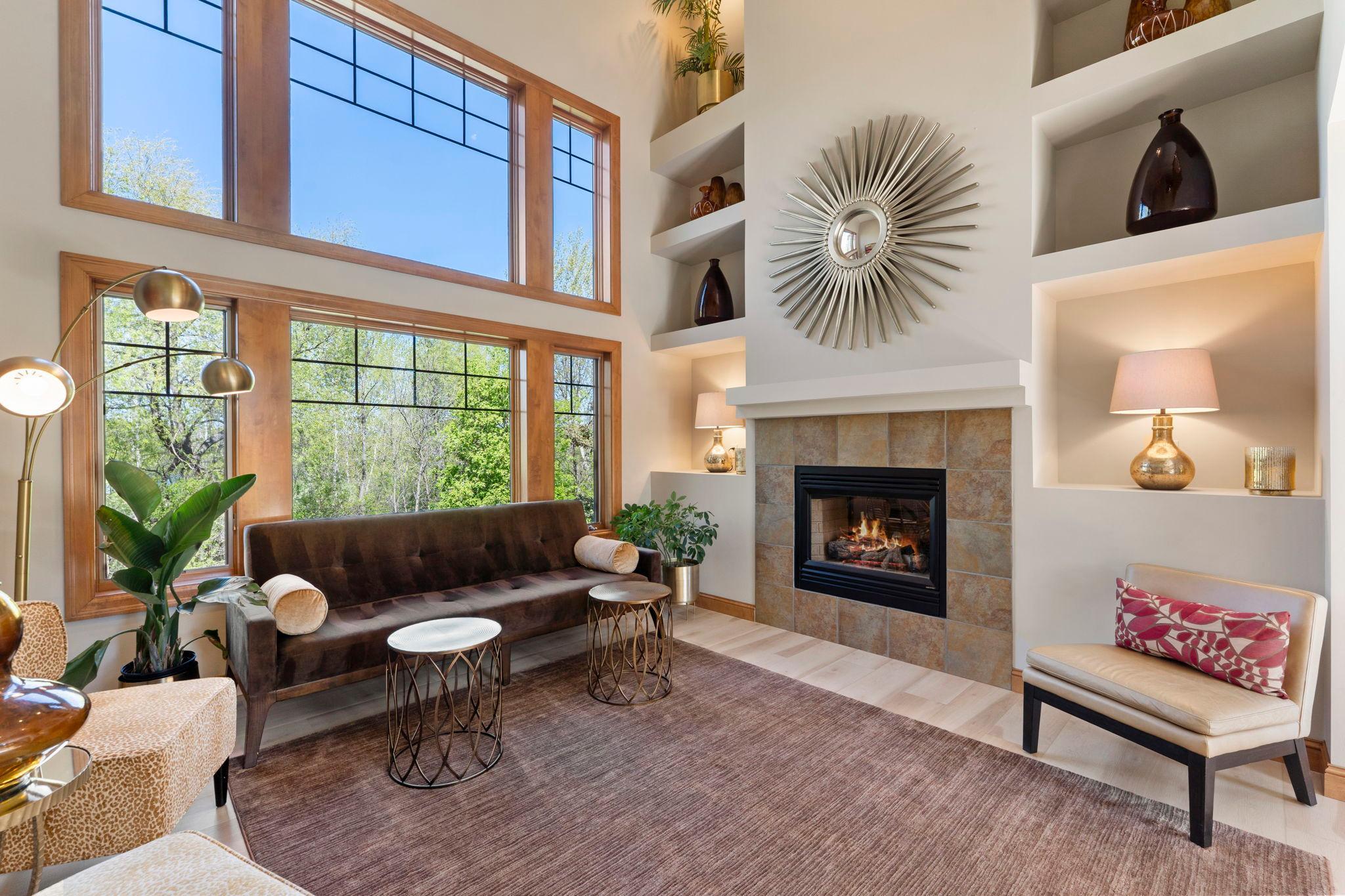 A cozy double-sided gas fireplace with tile surround and floor-to-ceiling shelving creates a beautiful focal point, while large windows fill the space with abundant natural light.