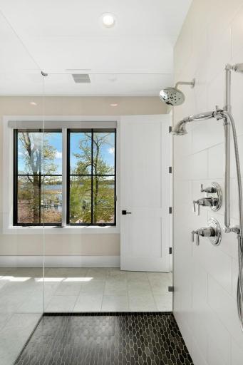 Offering heated floors, a spacious double vanity with ample storage, and a large glass-and-tile shower featuring three shower heads, including a rainfall option.