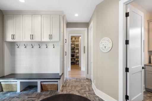 This functional space showcases distinctive Italian tile flooring, a built-in bench with cabinets and hooks for organization, a built-in desk, access to the front porch, and a 7x5 walk-in closet for additional storage.