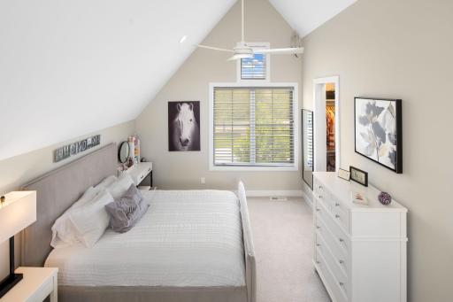 It features vaulted ceilings, a ceiling fan, walk-in closet, cozy carpeting, large windows that bring in abundant natural light, and a stylish hanging chandelier.