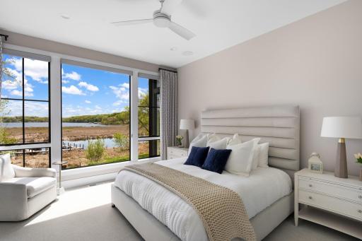 The main level also hosts the serene primary suite, featuring plush carpeting, a large picture window with beautiful lake views, abundant natural light, a ceiling fan, and a cozy gas fireplace with a quartz surround.