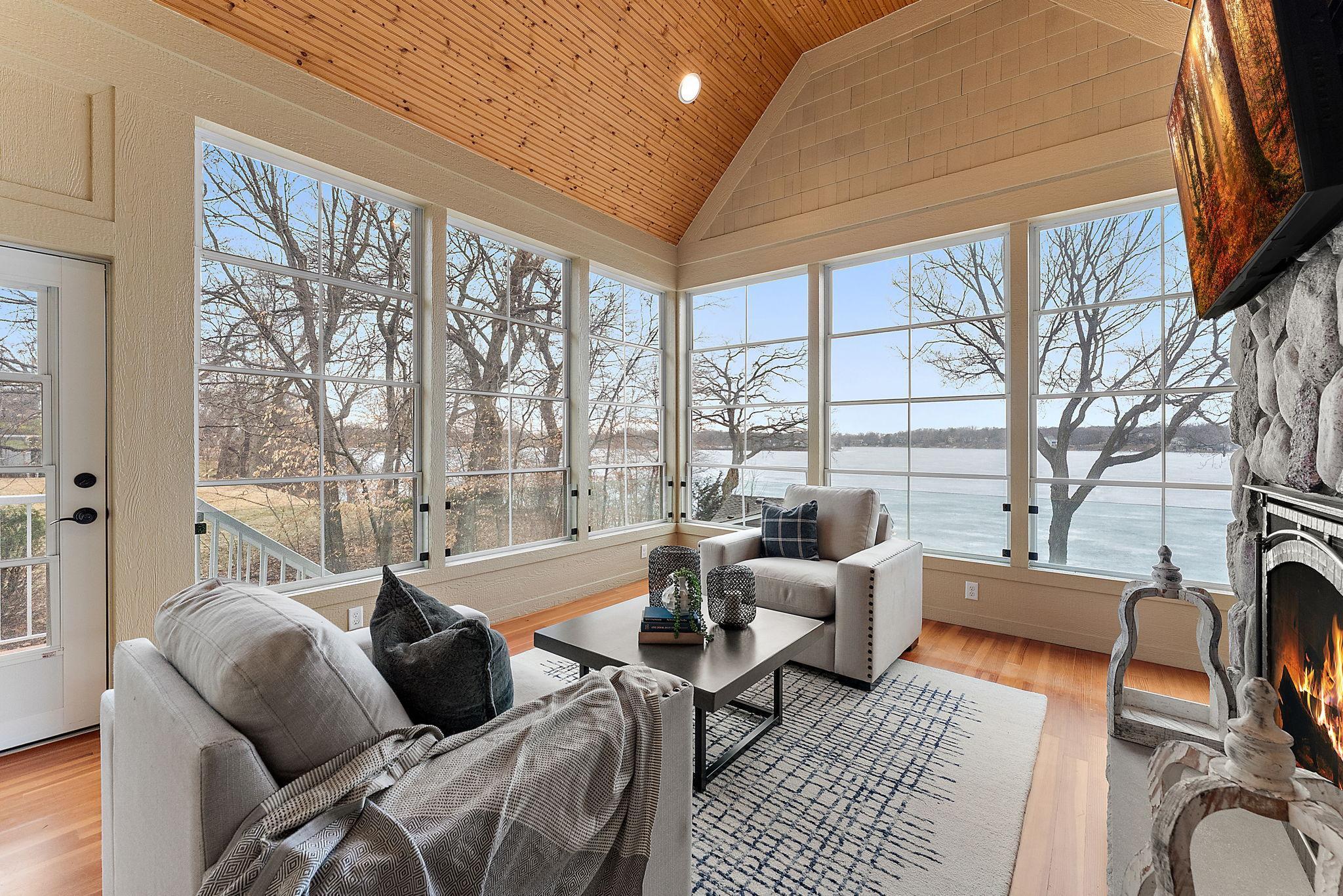 Main-level sunroom with vaulted wood ceiling, stone gas fireplace, and breathtaking views of the lake