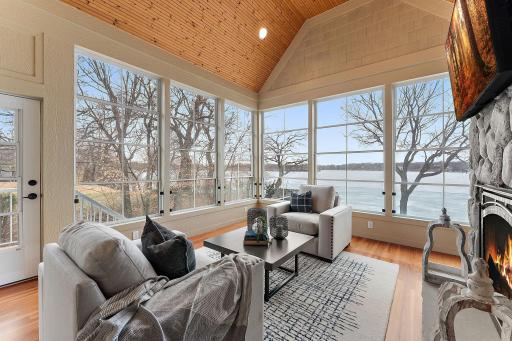 Main-level sunroom with vaulted wood ceiling, stone gas fireplace, and breathtaking views of the lake