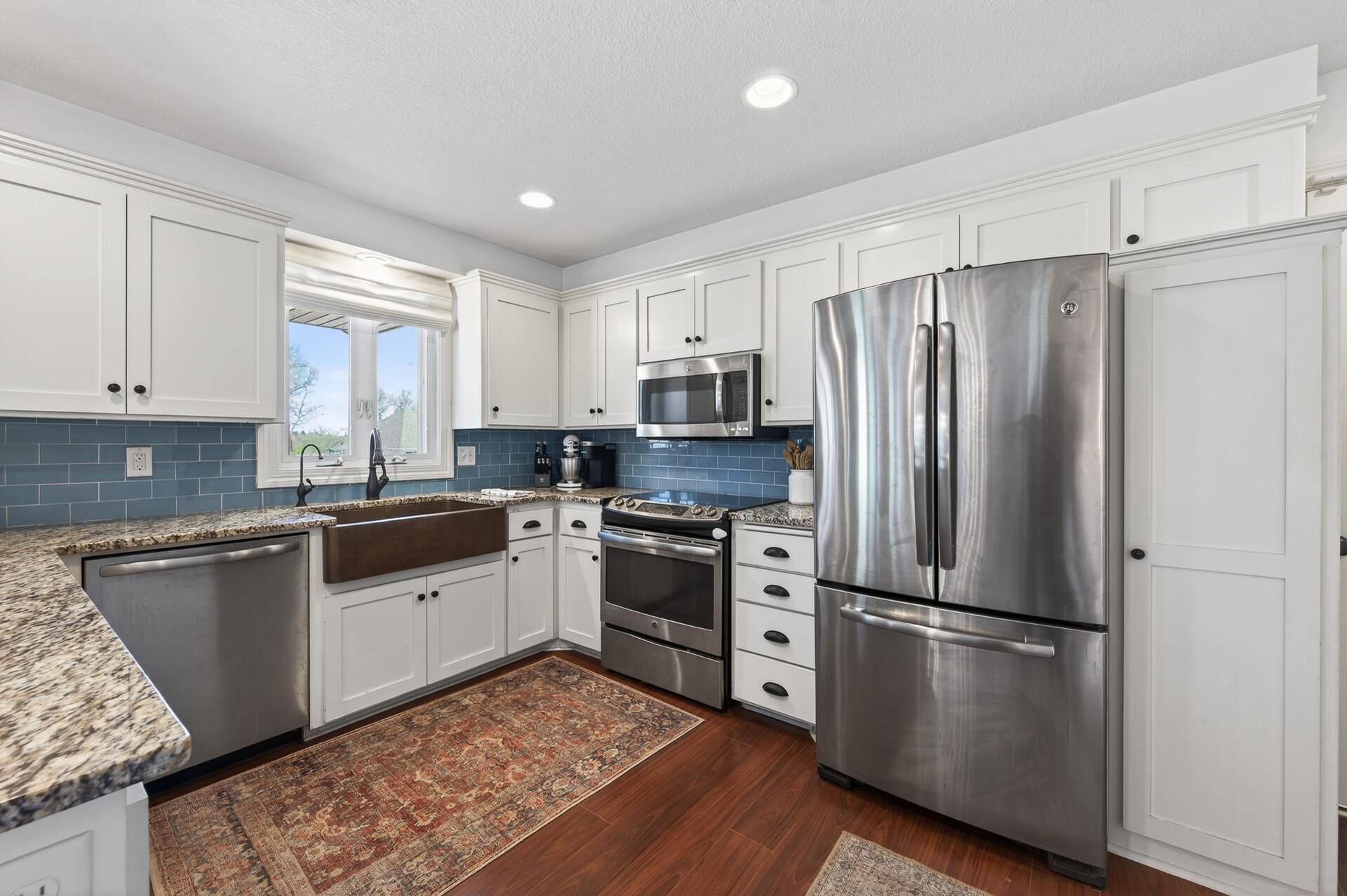 This entire kitchen is a dream from upgraded stainless appliances, dark laminate flooring, white cabinetry and trim, blue subway tile backsplash and granite counters, plus farm style single basin sink and loads of recessed lights.