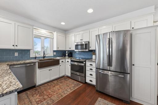 This entire kitchen is a dream from upgraded stainless appliances, dark laminate flooring, white cabinetry and trim, blue subway tile backsplash and granite counters, plus farm style single basin sink and loads of recessed lights.