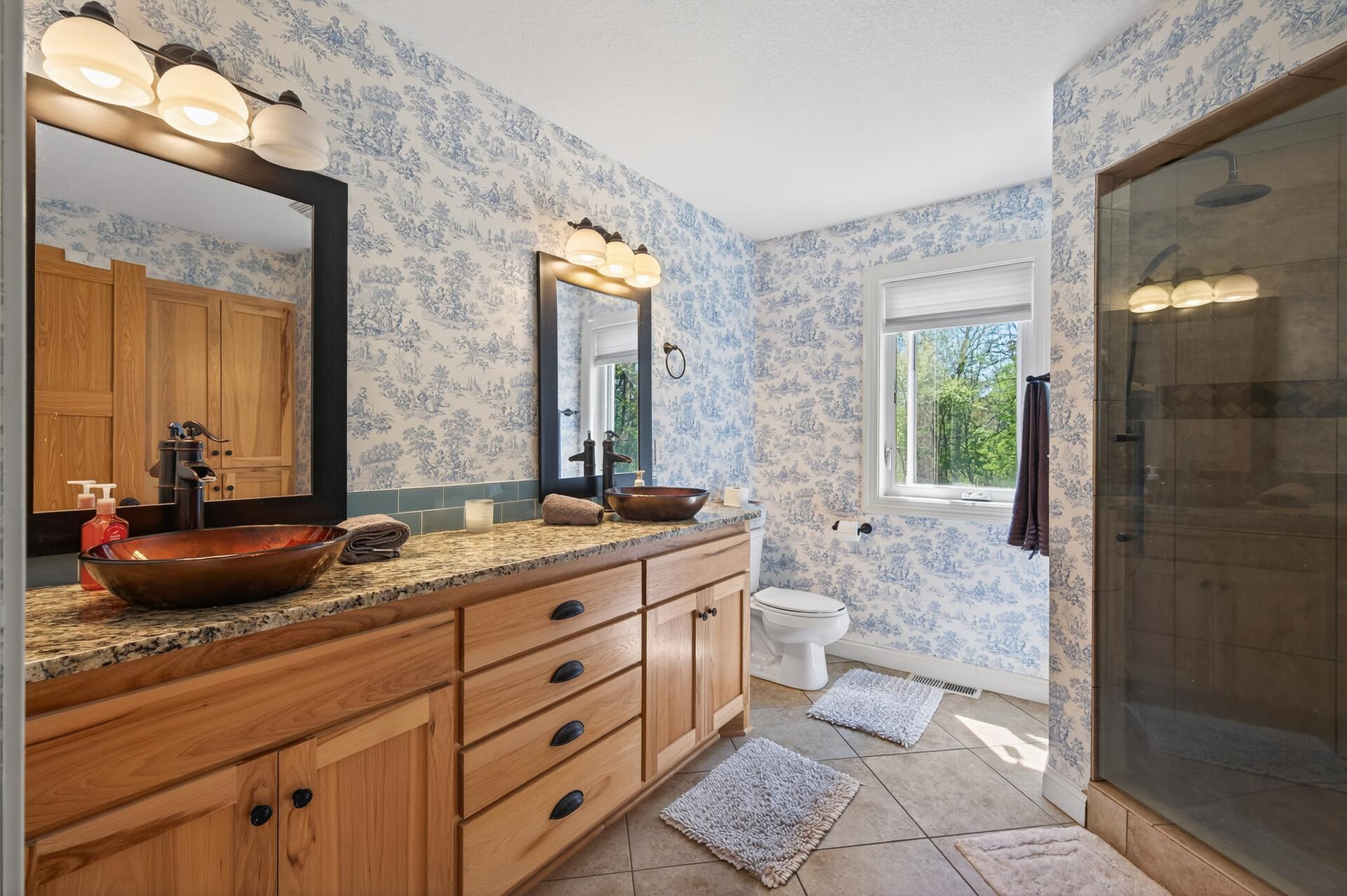 The private primary bath features a large walk-in fully tiled shower with dual heads and tiled seat & floor. There is a double vanity with granite top, vessel sinks, framed mirror and Hickory cabinets, plus linen closet.
