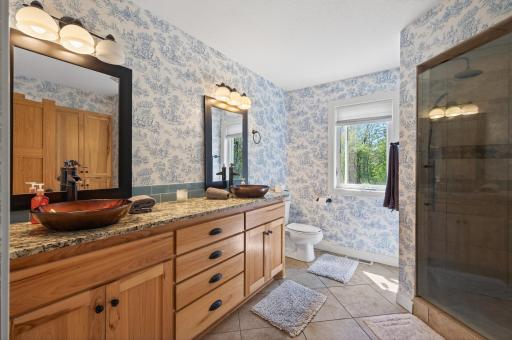 The private primary bath features a large walk-in fully tiled shower with dual heads and tiled seat & floor. There is a double vanity with granite top, vessel sinks, framed mirror and Hickory cabinets, plus linen closet.