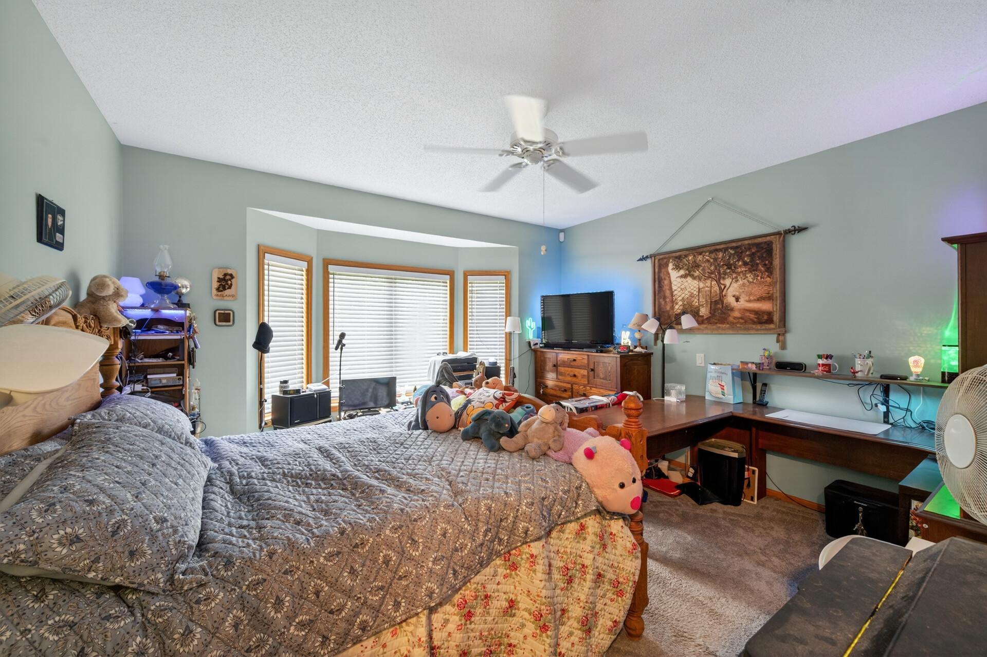 Primary bedroom is generous in size with plush carpeting, a bay window, and ceiling fan for added comfort.