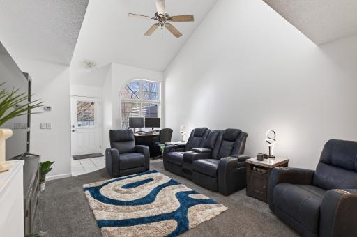 The living room boasts soaring vaulted ceilings with neutral tones and a ceiling fan for added comfort.