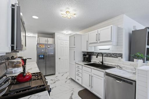 The kitchen offers crisp white cabinetry, marbled tile flooring, stainless steel appliances, and a tiled backsplash.