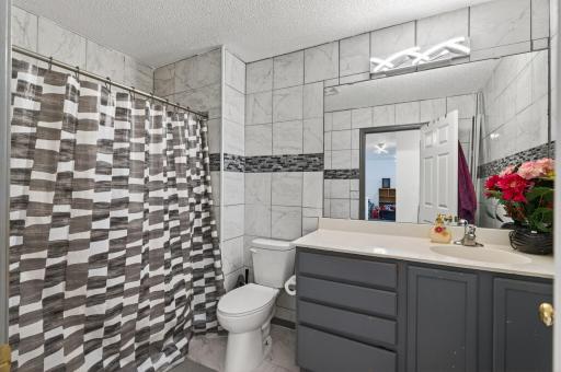 A moody gray vanity paired with tile finishes and a tub/shower combo creates a stylish, functional space.