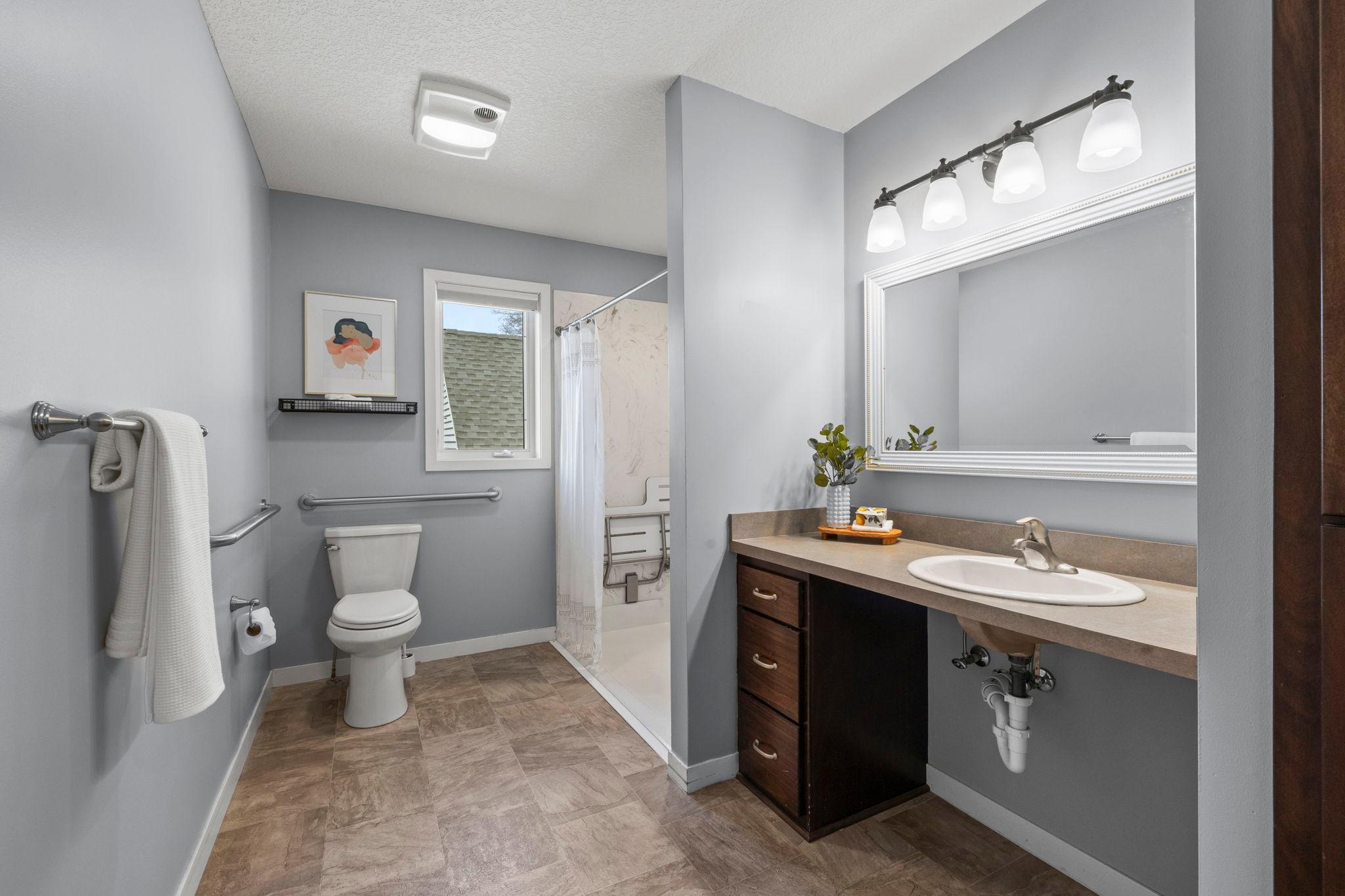 A nearby full bathroom includes a roll-in shower, linen cabinetry, and additional hall storage.