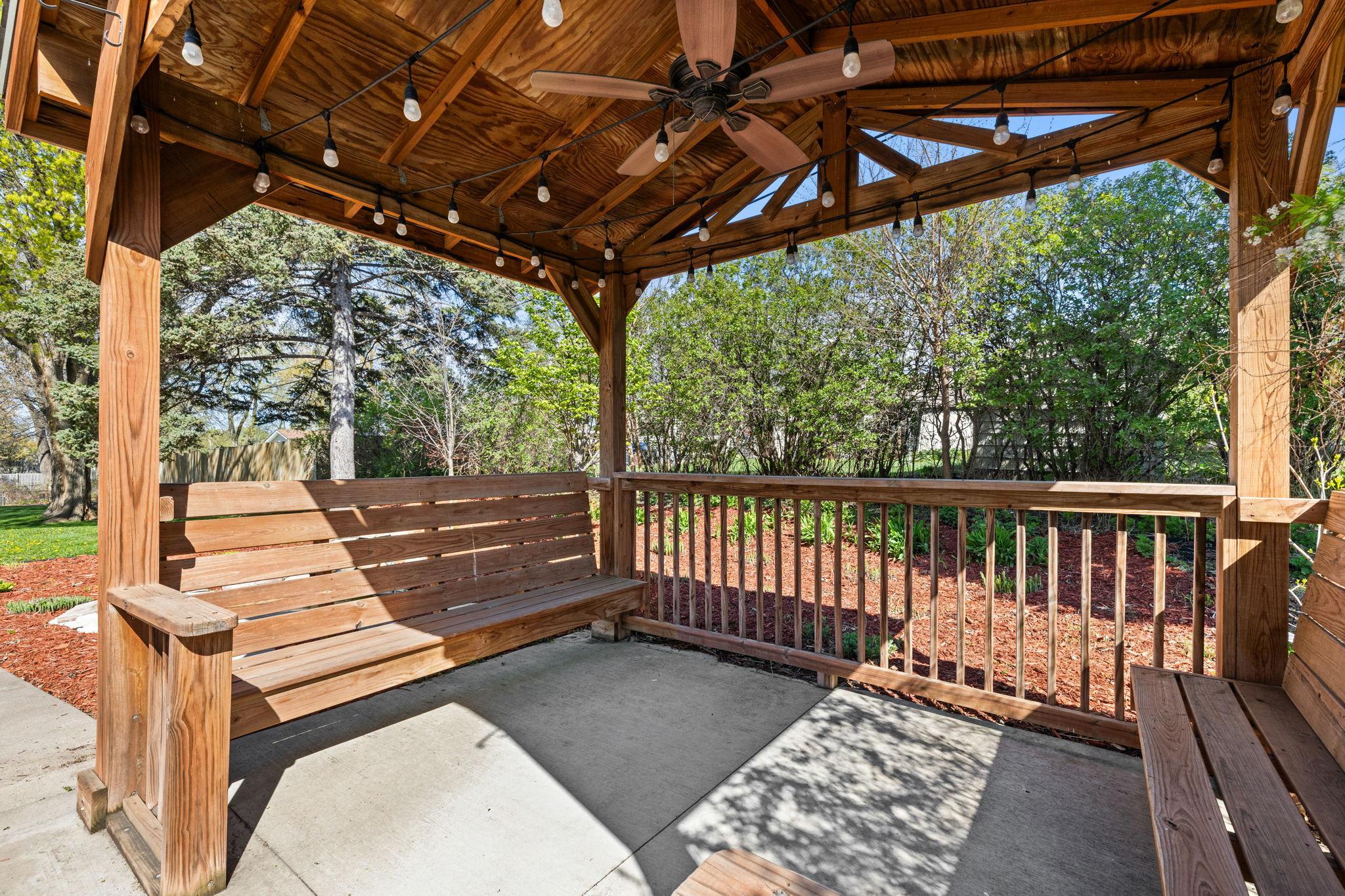 A built-in wood gazebo with lighting and bench seating creates a welcoming retreat for outdoor enjoyment.
