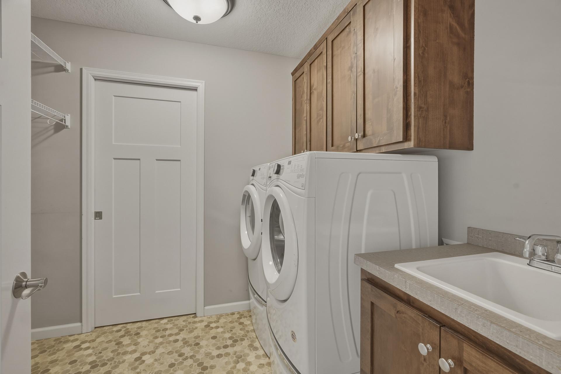 Laundry room with full sized washer/dryer, upper cabinets and sink.