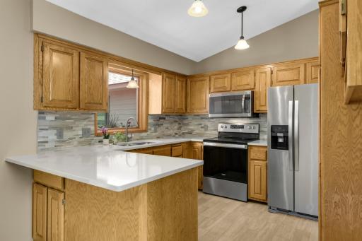 Tile backsplash, tiled flooring, and warm oak wood cabinetry with ample storage.