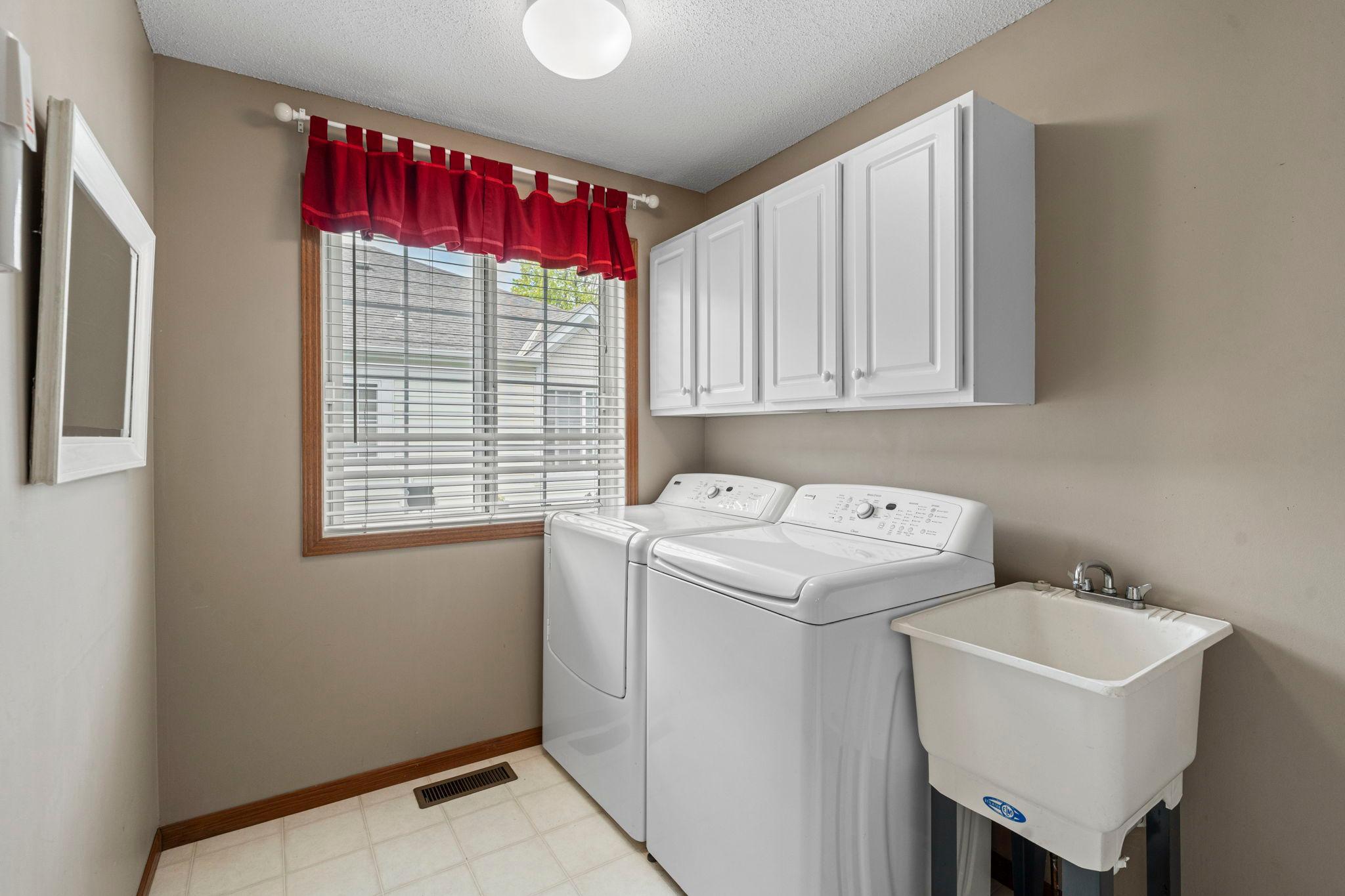 Main floor laundry room right off the kitchen has convenient white cabinets and a handy laundry tub.