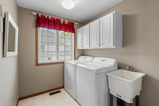 Main floor laundry room right off the kitchen has convenient white cabinets and a handy laundry tub.