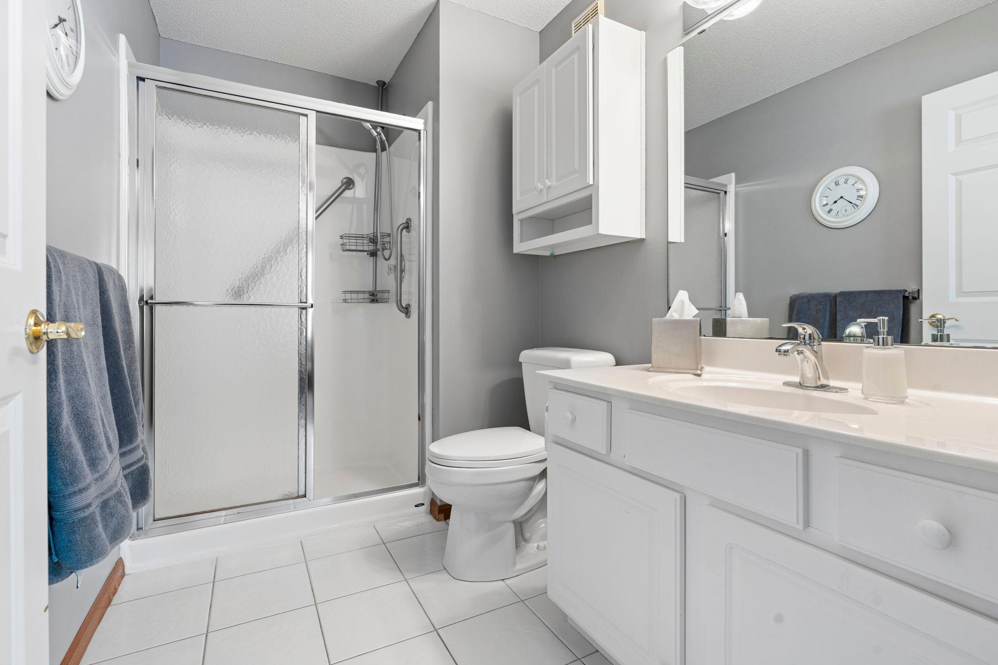 Primary bedroom has it's own bathroom with step-in shower and white cabinetry.