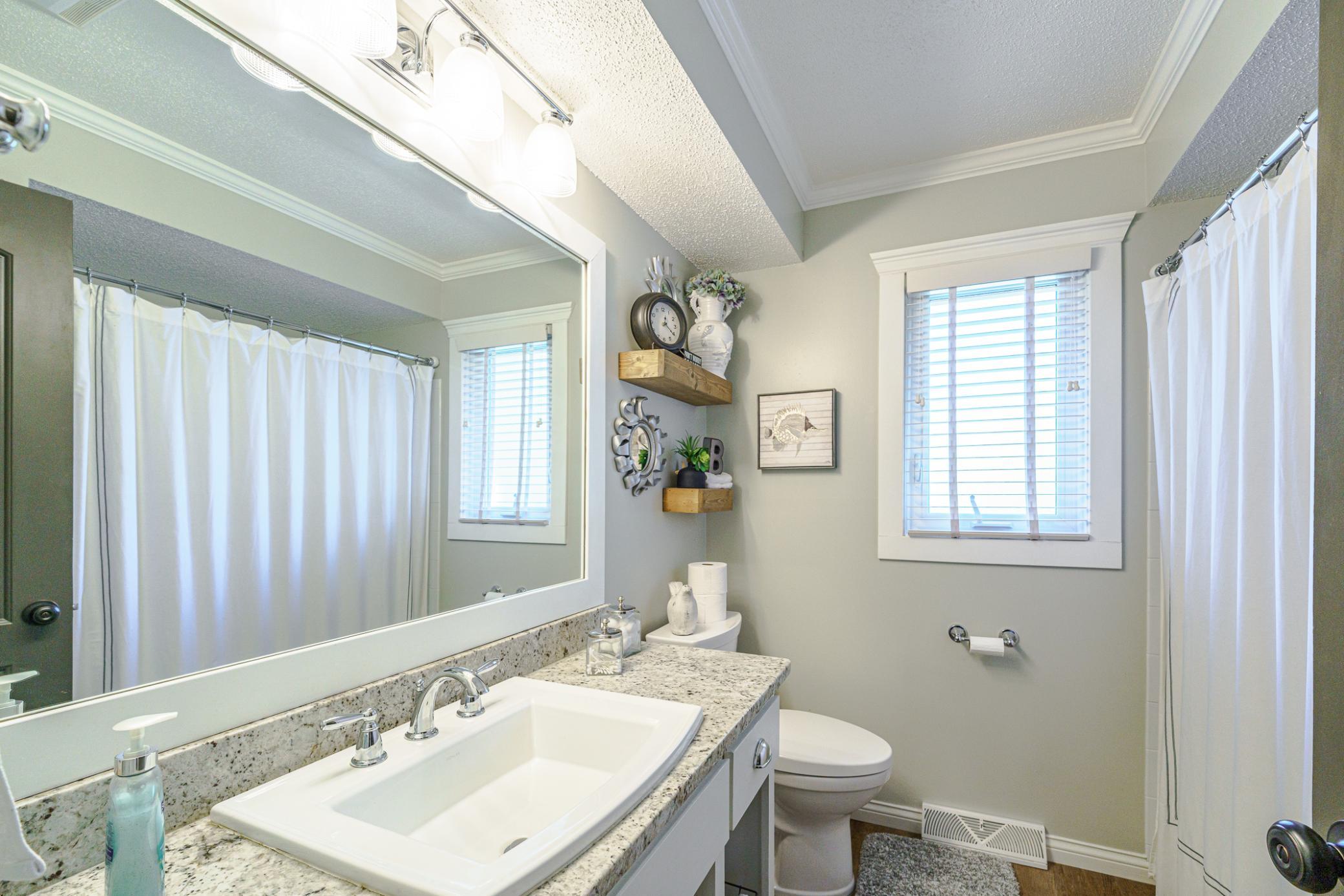 The full bath that services the bedrooms has wood-style flooring, a furniture-style vanity, granite surfaces, crown molding and a framed mirror.