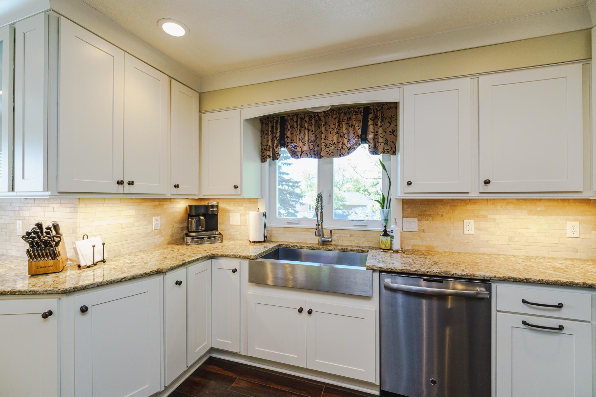 Granite countertops and a travertine backsplash dress up this space. The stainless steel sink has a gooseneck faucet and overlooks the backyard.