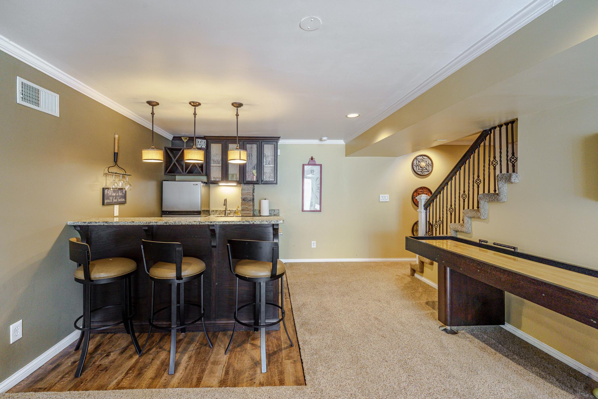 The wet bar has granite countertops and cabinetry with rain glass door fronts. Three pendant lights hang above the bar.