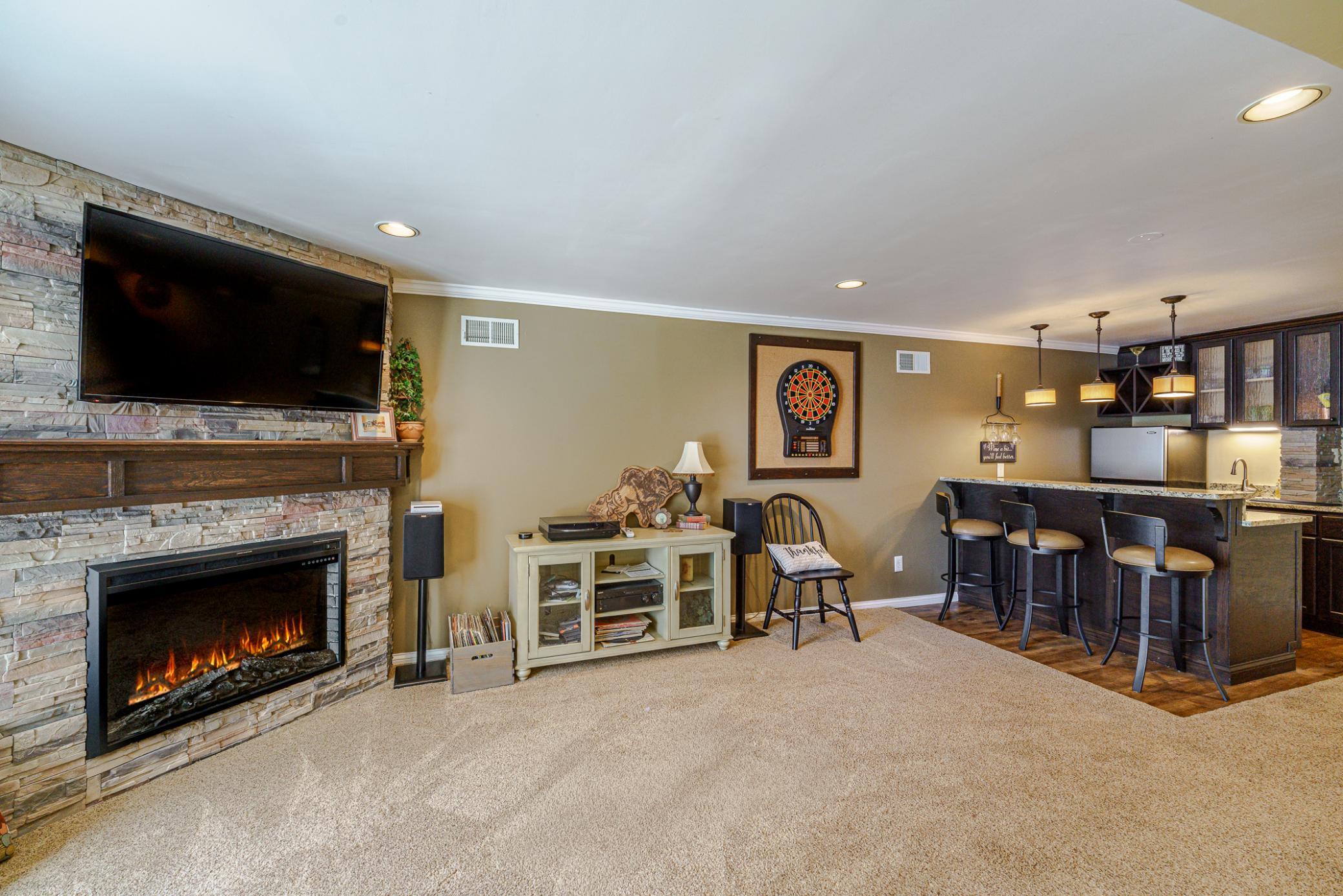 Cozy lower level family room, with a custom mantle on the fireplace. At the bar, there is a sink, and all the pipes coming into the bar are concealed in a stonework column.