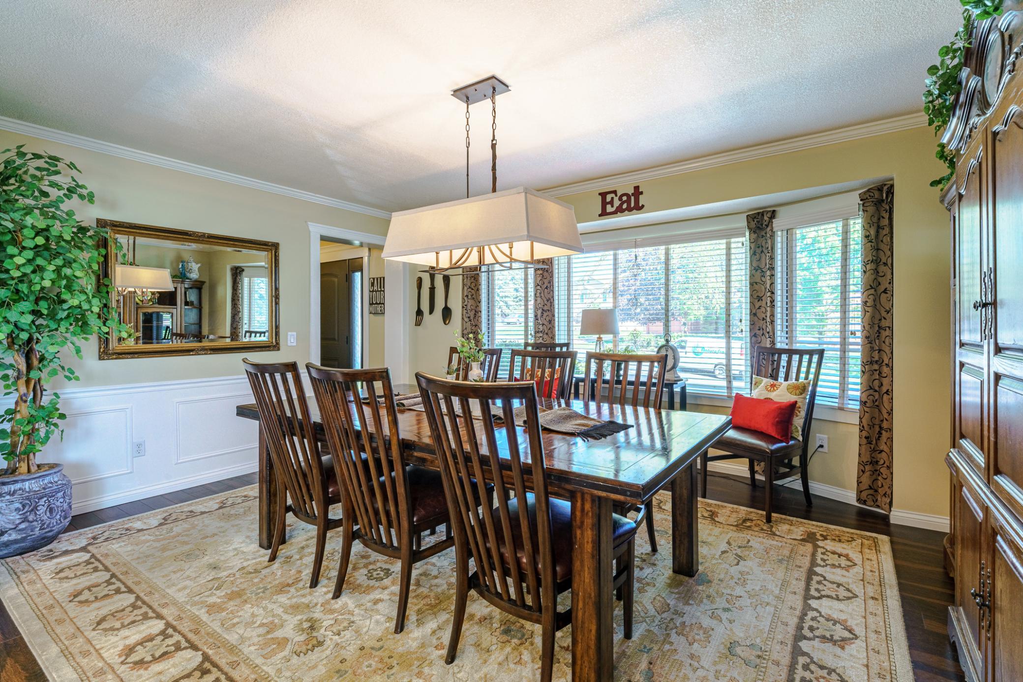 The dining room lies off the kitchen and includes wood flooring and bay windows. Paneled wall details and crown molding add elegance to this space. The horizontal chandelier suits the room layout perfectly.
