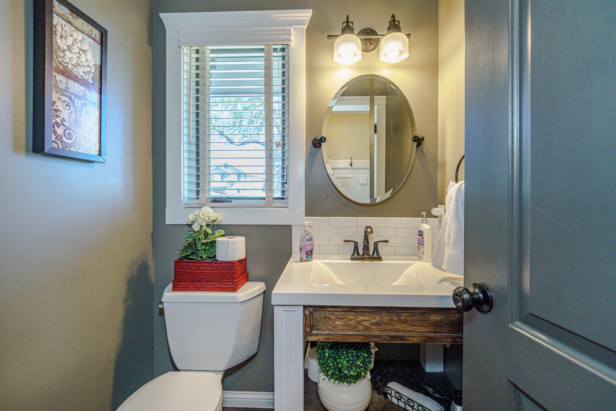 The half bath has hardwood flooring, wall paneling, and a custom vanity with subway tile and an oval mirror. The half bath lies off the rear hall.