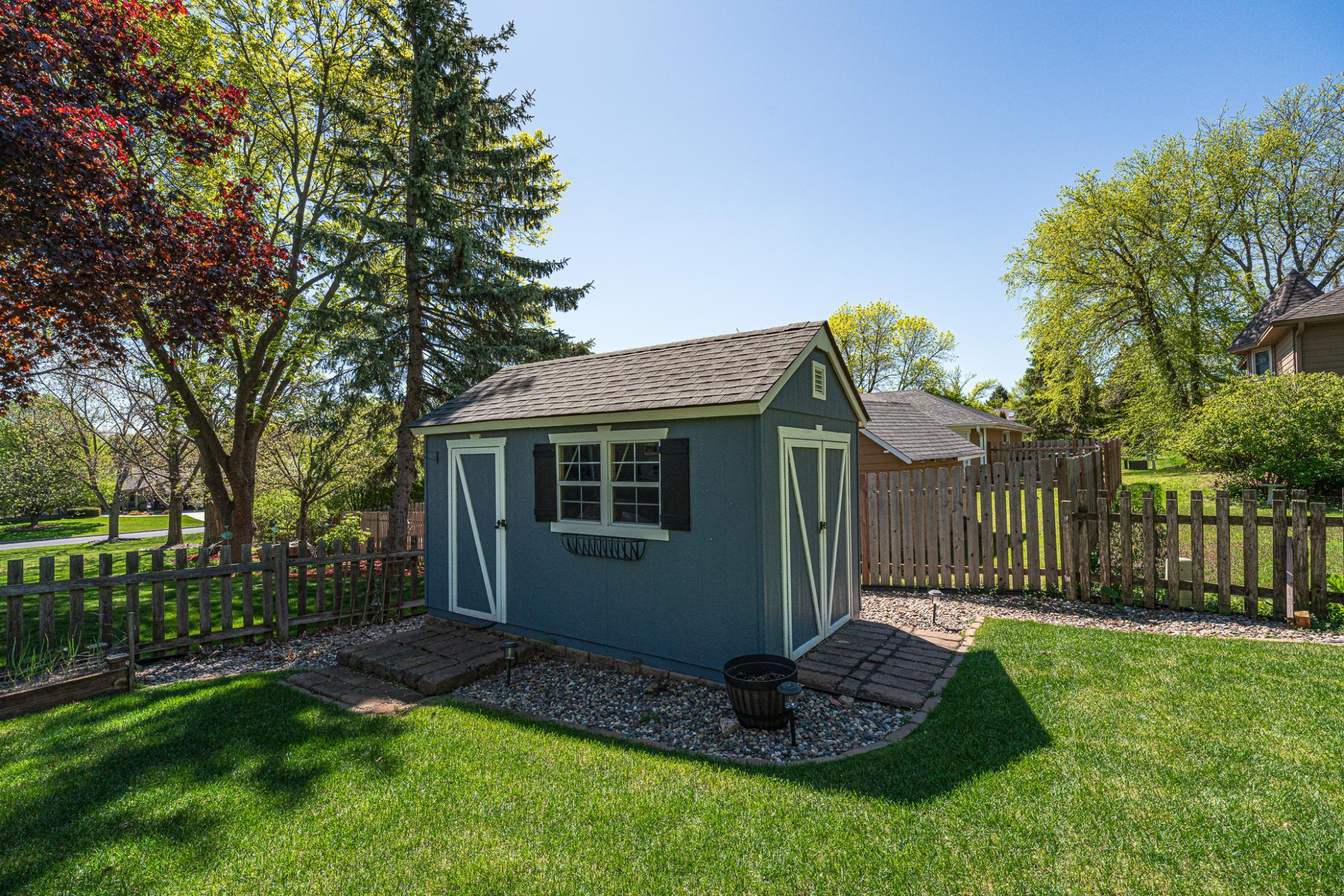 The shed is landscaped and has windows and paver entry points.