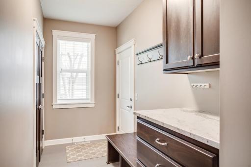 The thoughtfully designed mudroom includes custom built-ins, tile floors, granite counter, and a closet for added organization and convenience.