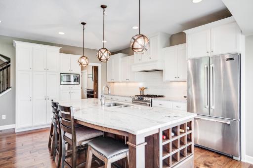 The stunning kitchen features granite countertops, subway tile backsplash, enameled cabinetry, stainless steel appliances, and an oversized center island with seating and built-in wine storage.
