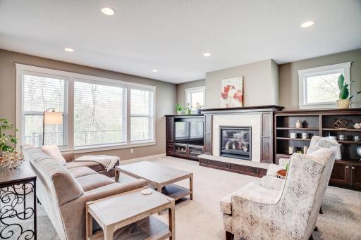 The inviting great room showcases a focal gas fireplace flanked by custom built-ins and expansive windows that fill the space with natural light while overlooking the treed backyard views.