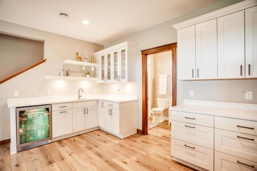 The adjoining bar area is exceptionally well-equipped with quartz countertops, beverage fridge, sink, abundant cabinetry, display shelving, and generous serving space.