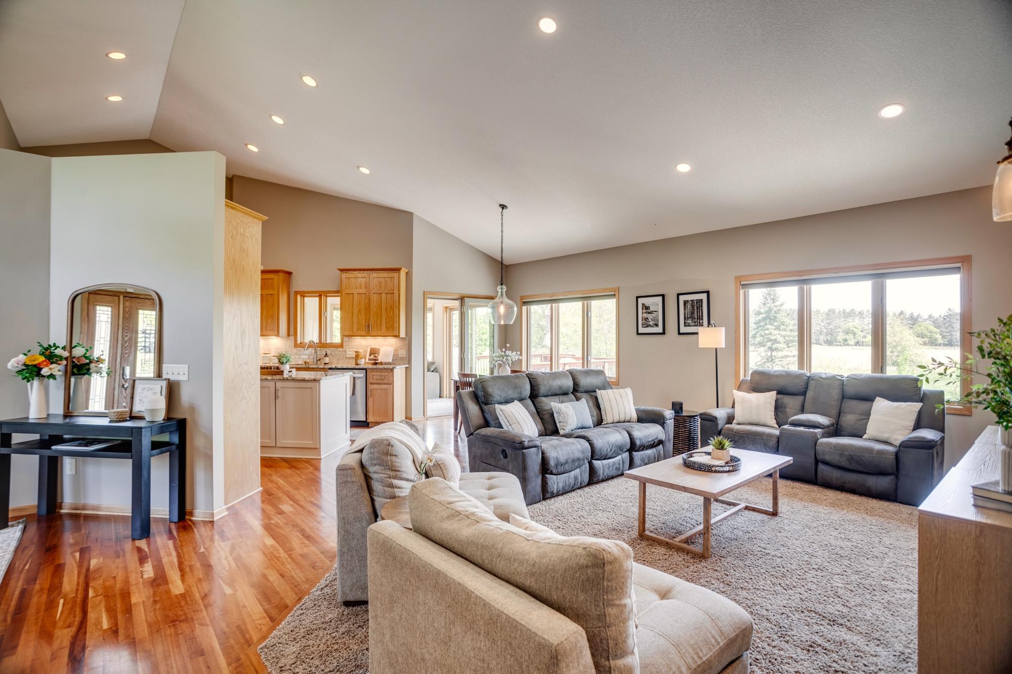 The main level features an open floor plan, hardwood floors, vaulted ceilings, and a wall of windows overlooking the patio and surrounding landscape