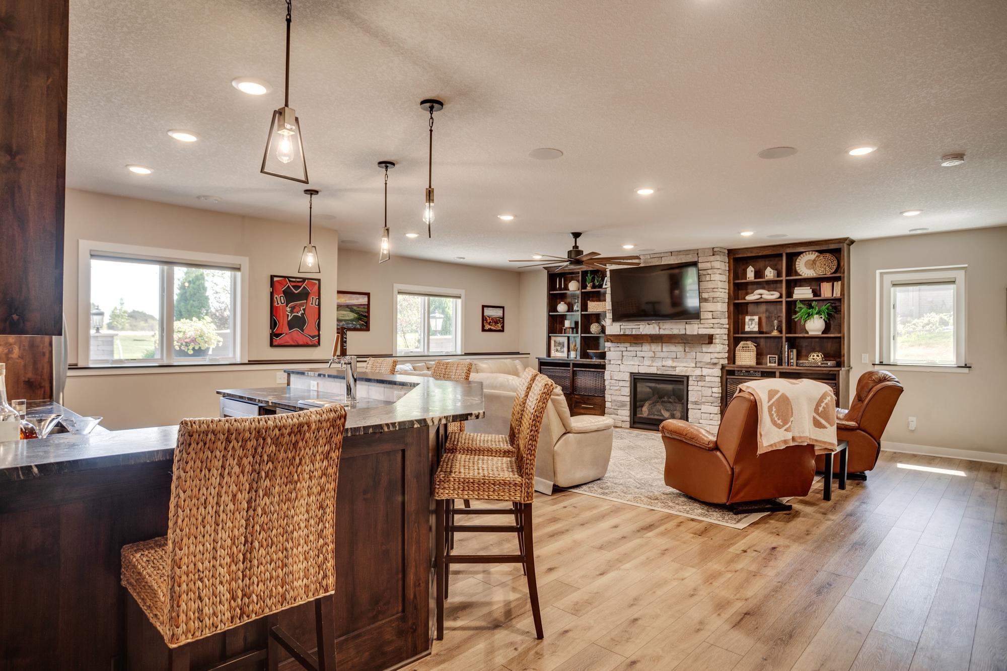 Spacious lower-level family room centered around a beautiful stone fireplace, complete with a full-size bar and kitchenette