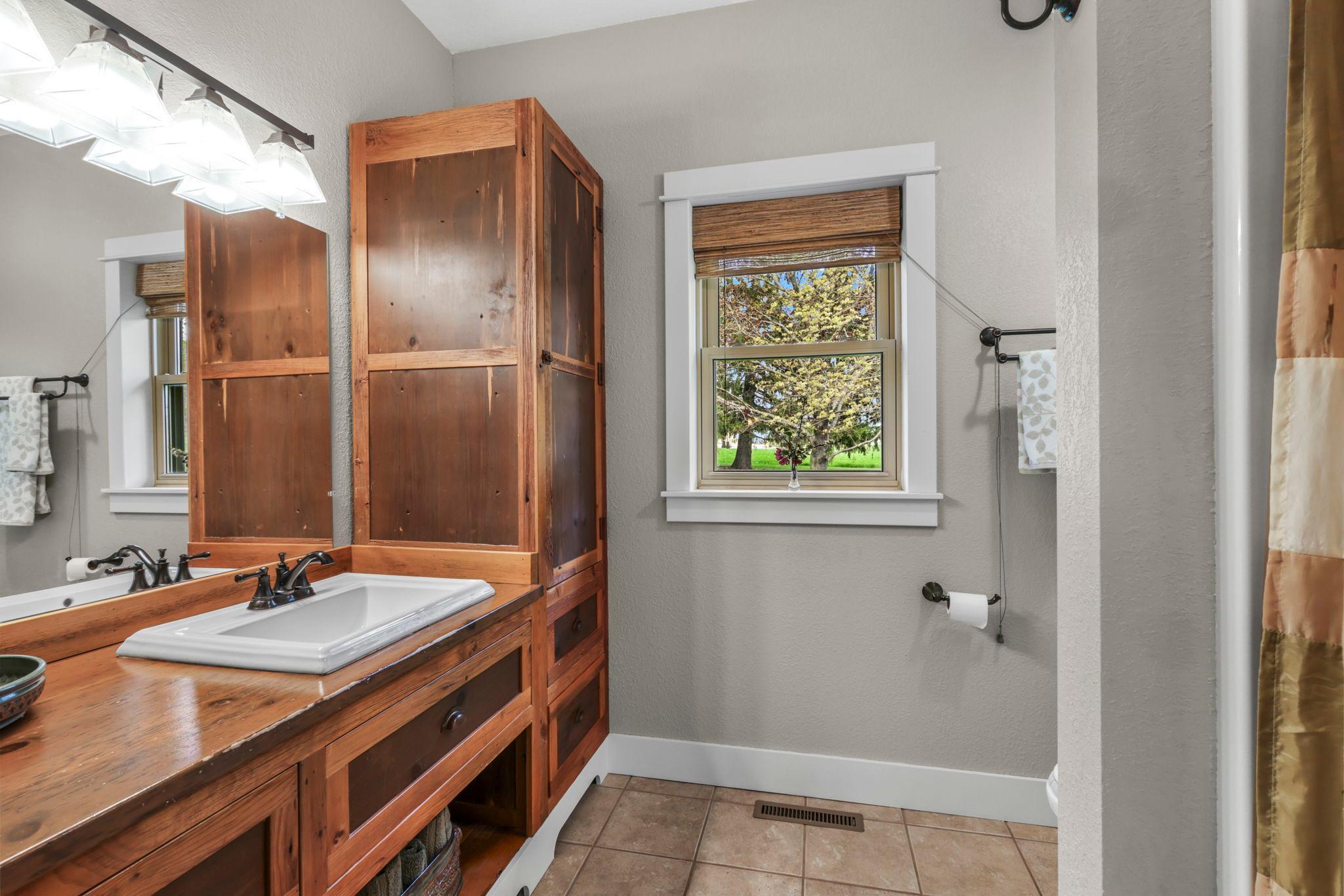 Rustic wood vanity and earthy finishes blend perfectly with the home’s cozy farmhouse character.