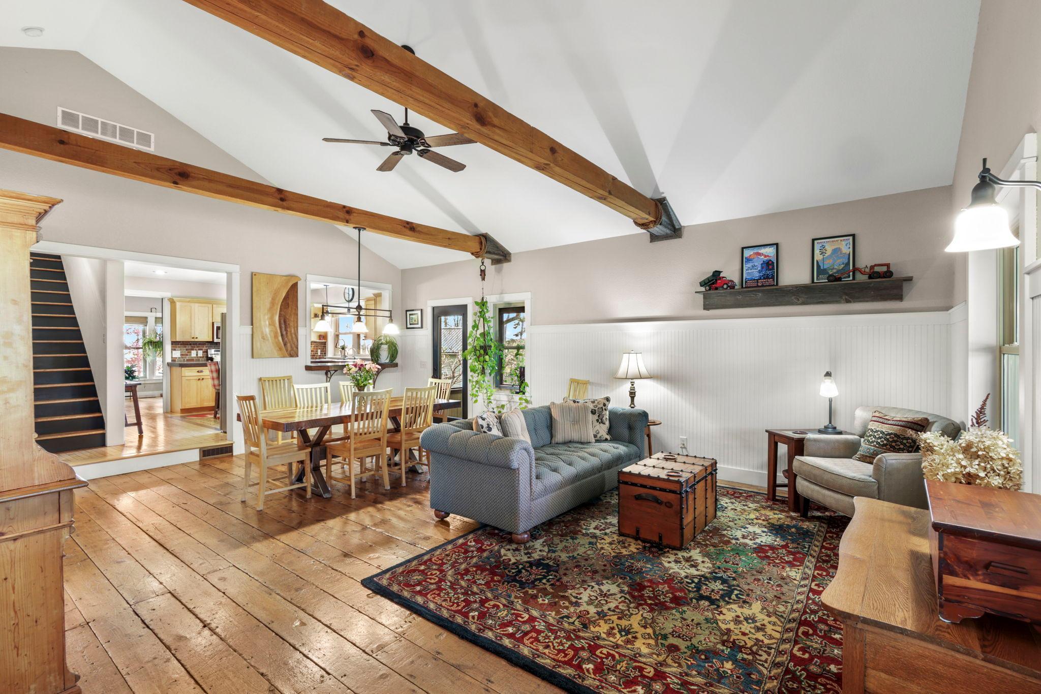 Spacious living and dining area with soaring vaulted ceilings, exposed wood beams, and rich hardwood floors.