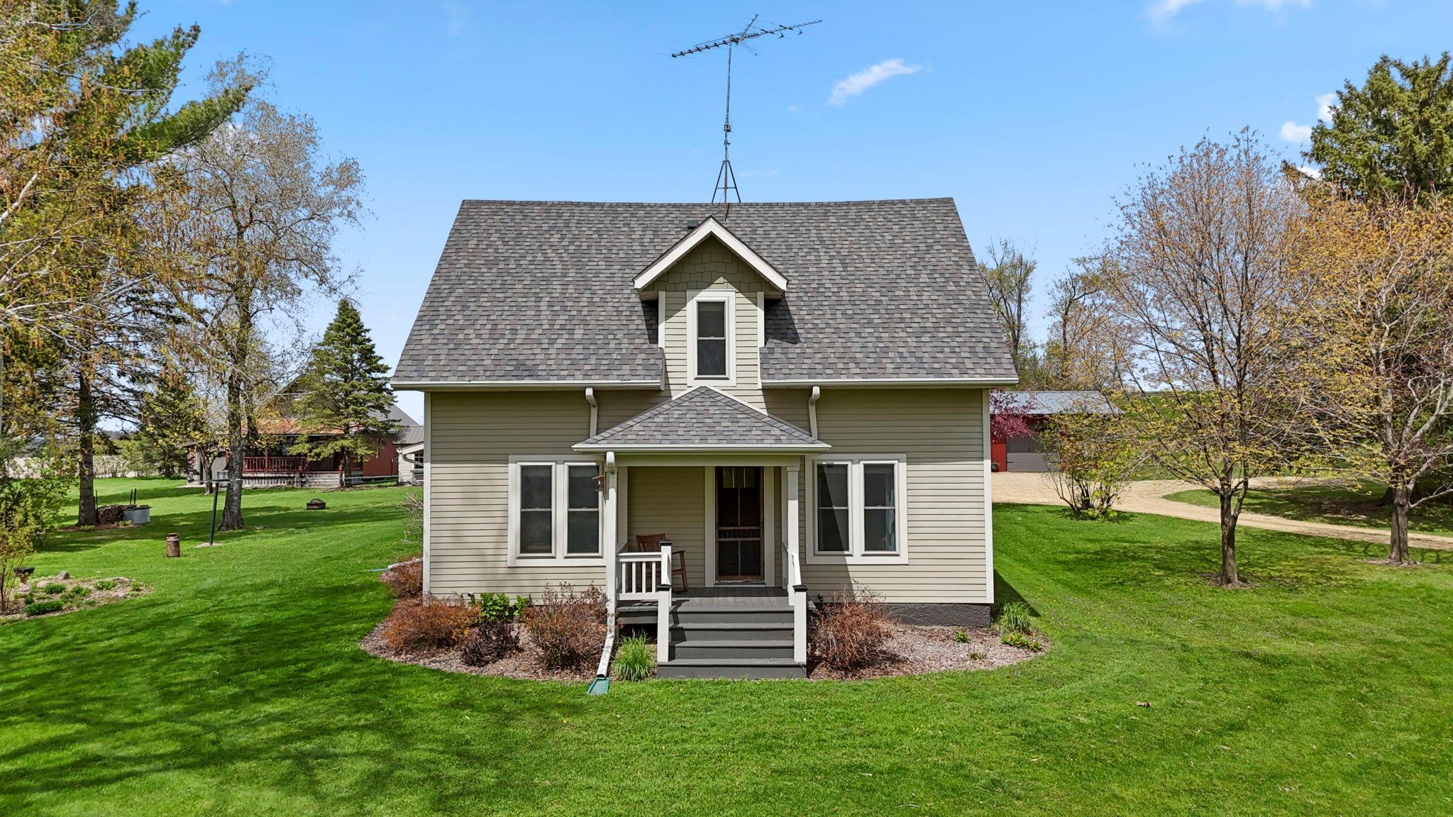 Charming farmhouse exterior nestled on a picturesque country setting with mature trees and wide-open green space.