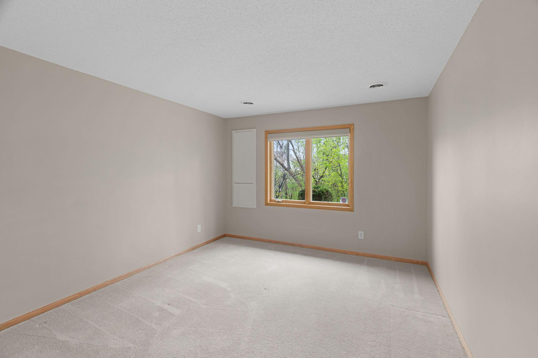 Spacious lower-level bedroom with large window and peaceful wooded backdrop.