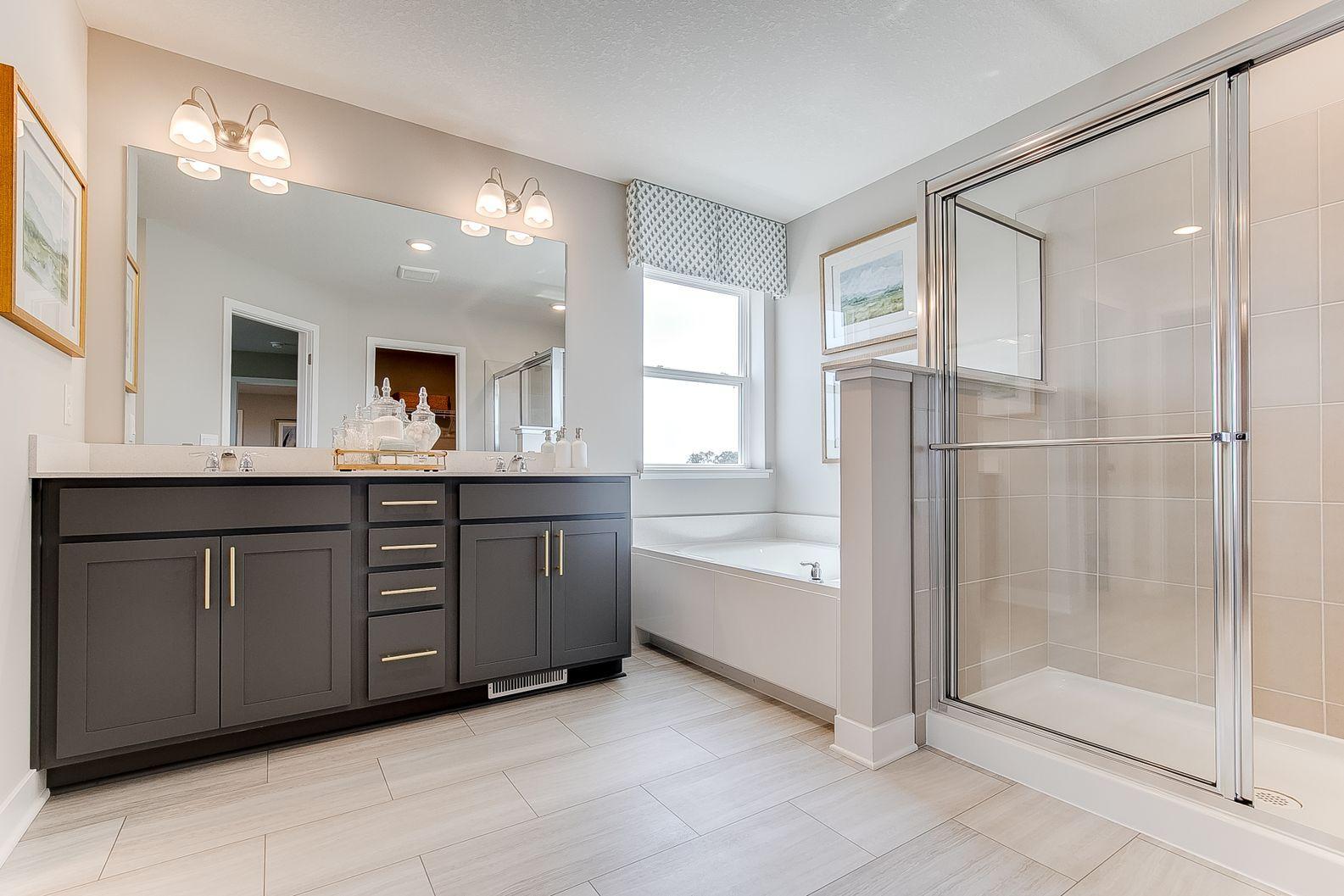 Convenient dual sinks, a relaxing soaking tub, beautiful luxury vinyl tile, and a walk-in shower in the primary en-suite bathroom. Photo of model home, colors and finishes are similar.
