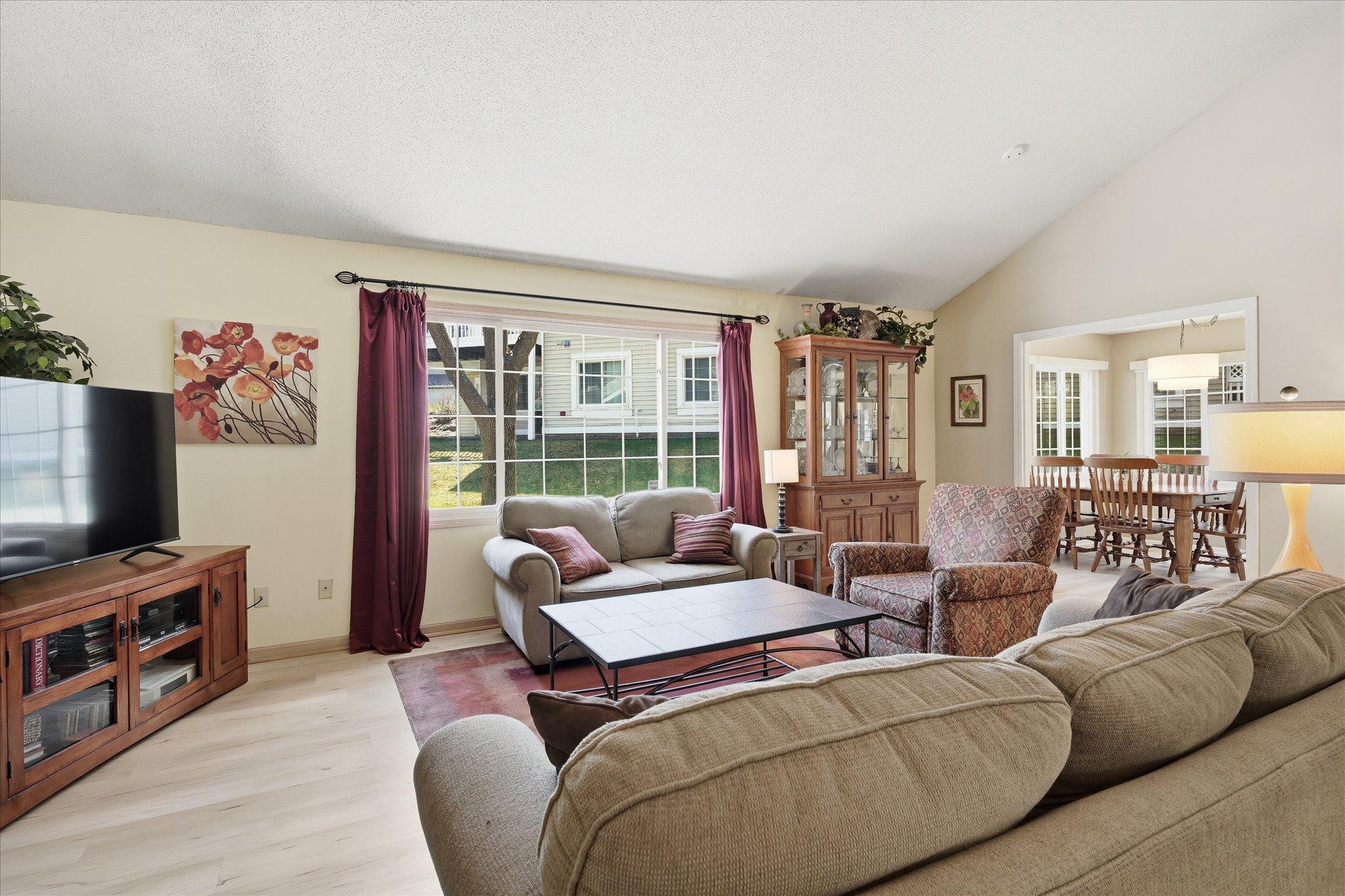 Bright and inviting living area with open flow to the dining space, featuring updated flooring and expansive windows.