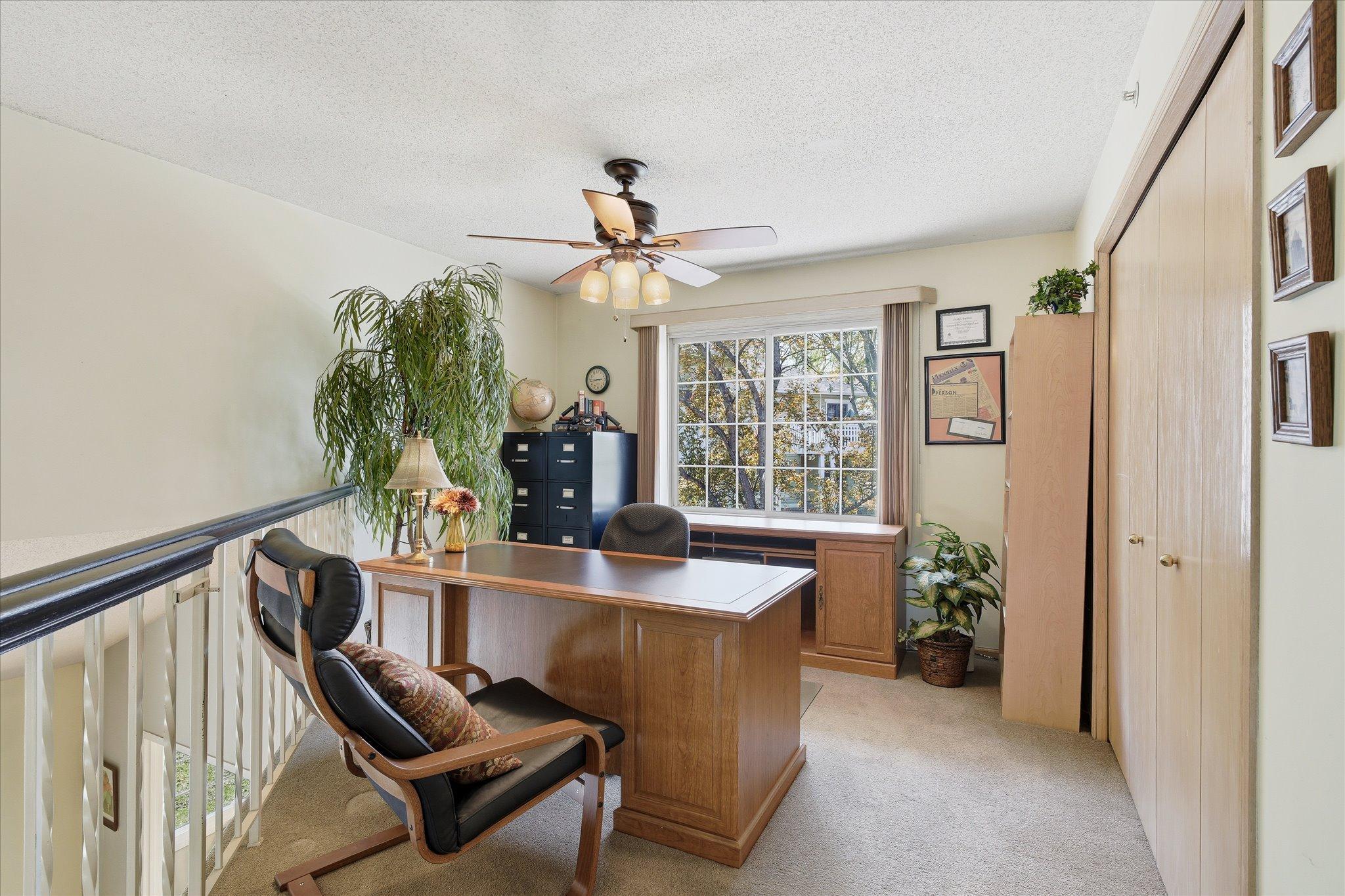 Bright upper-level loft/office space with vaulted ceiling, ceiling fan, and large window bringing in great natural light.