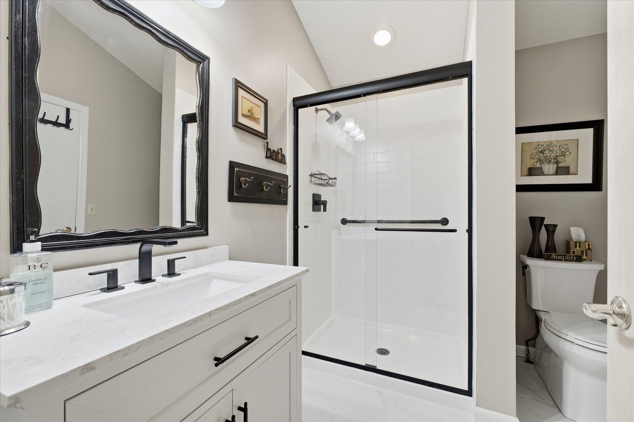Beautifully updated walk though bathroom featuring modern vanity, solid surface countertop, and tiled walk-in shower.