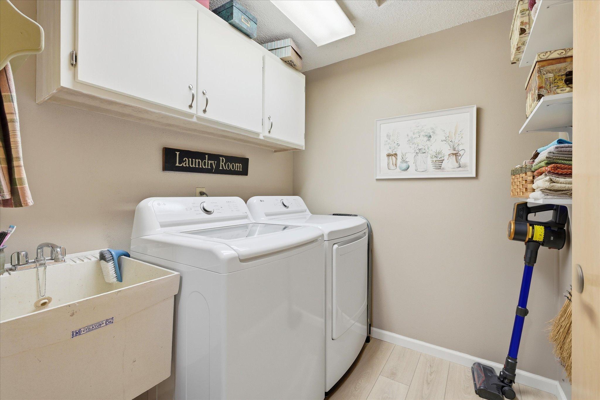 Convenient laundry room with washer, dryer, utility sink, and upper cabinetry.