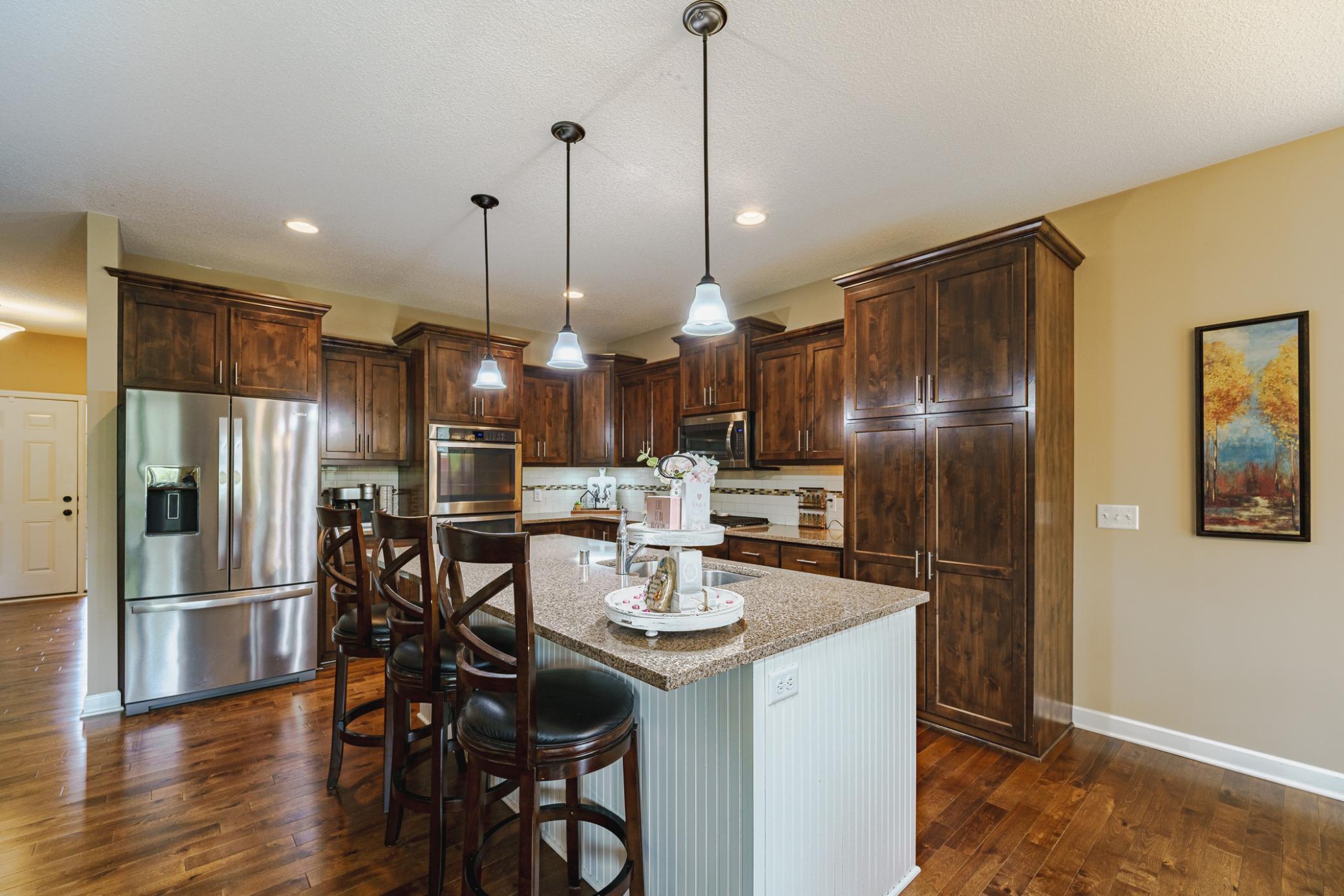 The kitchen includes quartz countertops and staggered 36” knotty alder cabinetry with roll-out shelves. The white wainscot center island contrasts with the wood perimeter cabinets.