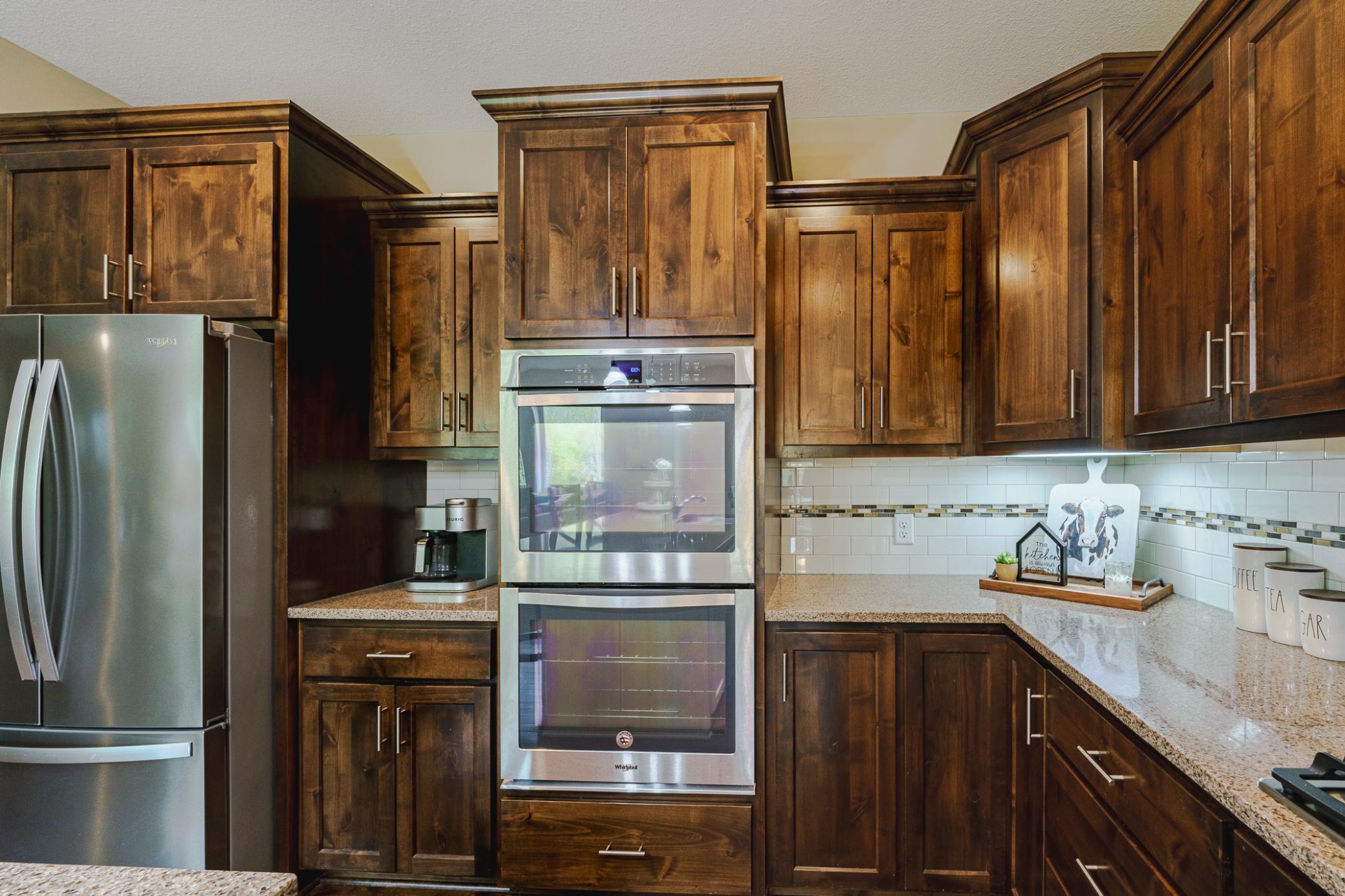 The subway tile backsplash is illuminated by undercabinet lighting. There is a wall oven as a part of the stainless appliance package.