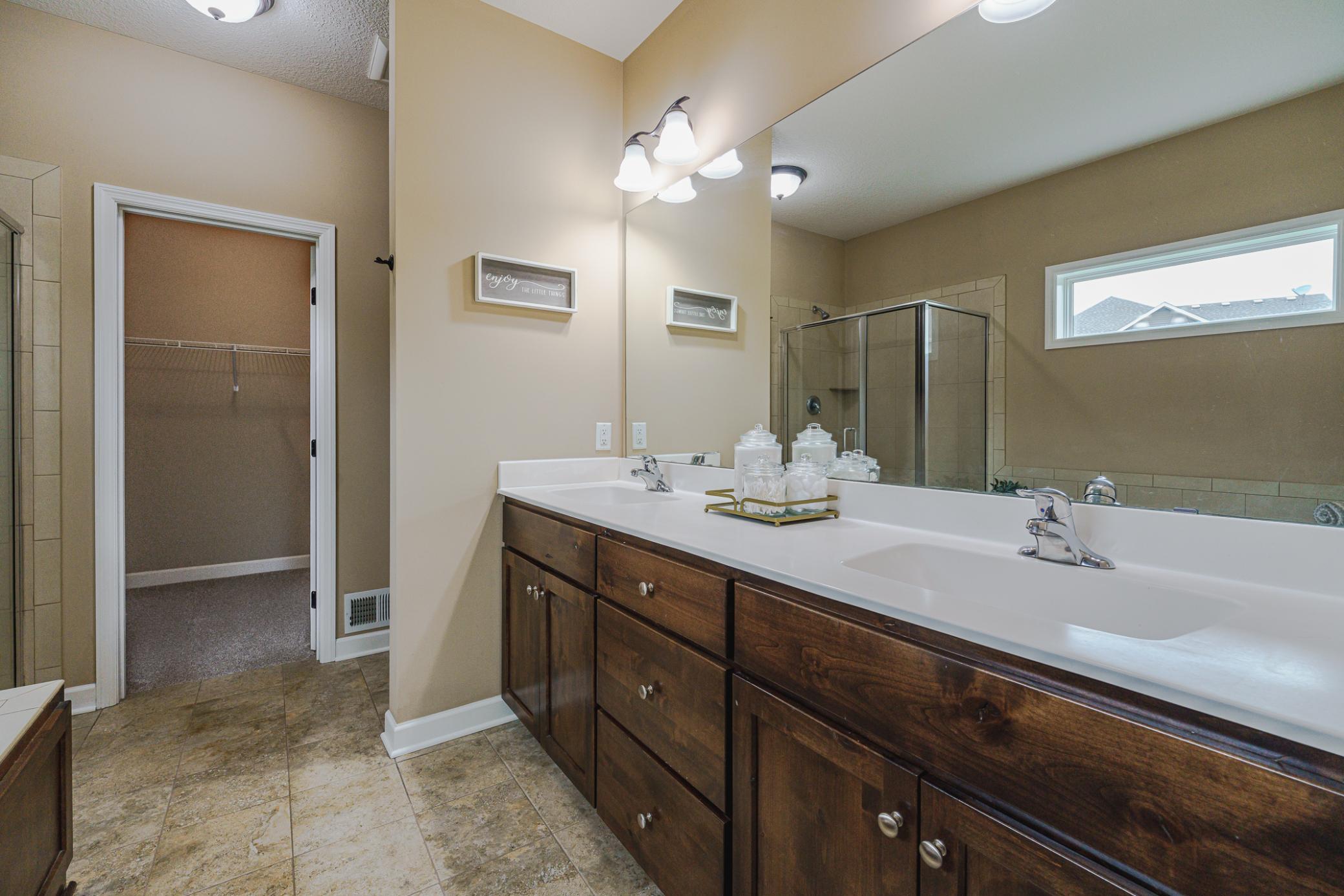 The adjoined bath is separated from the bedroom via a pocket door and includes tile flooring, a jetted tub, an elevated height dual-sink vanity, and a tile shower.